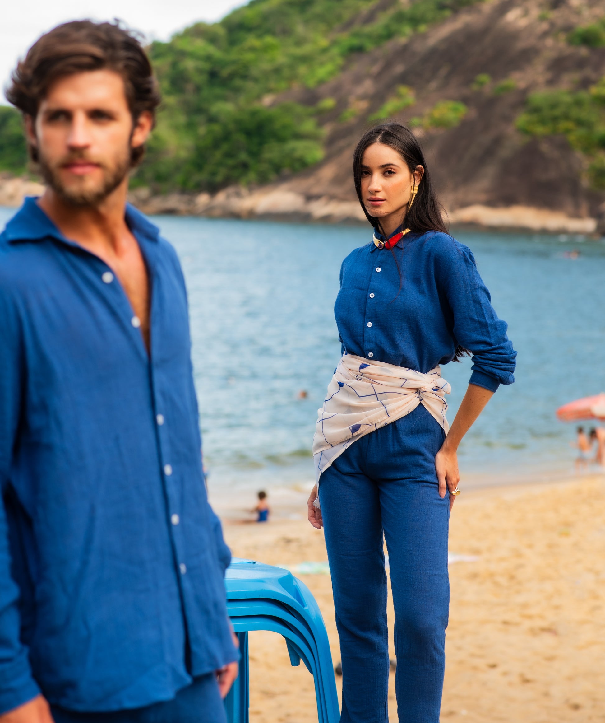 Modelo masculino vestindo full look com camisa manga longa e calça azul marinho unissex, posando sentado ao ar livre.