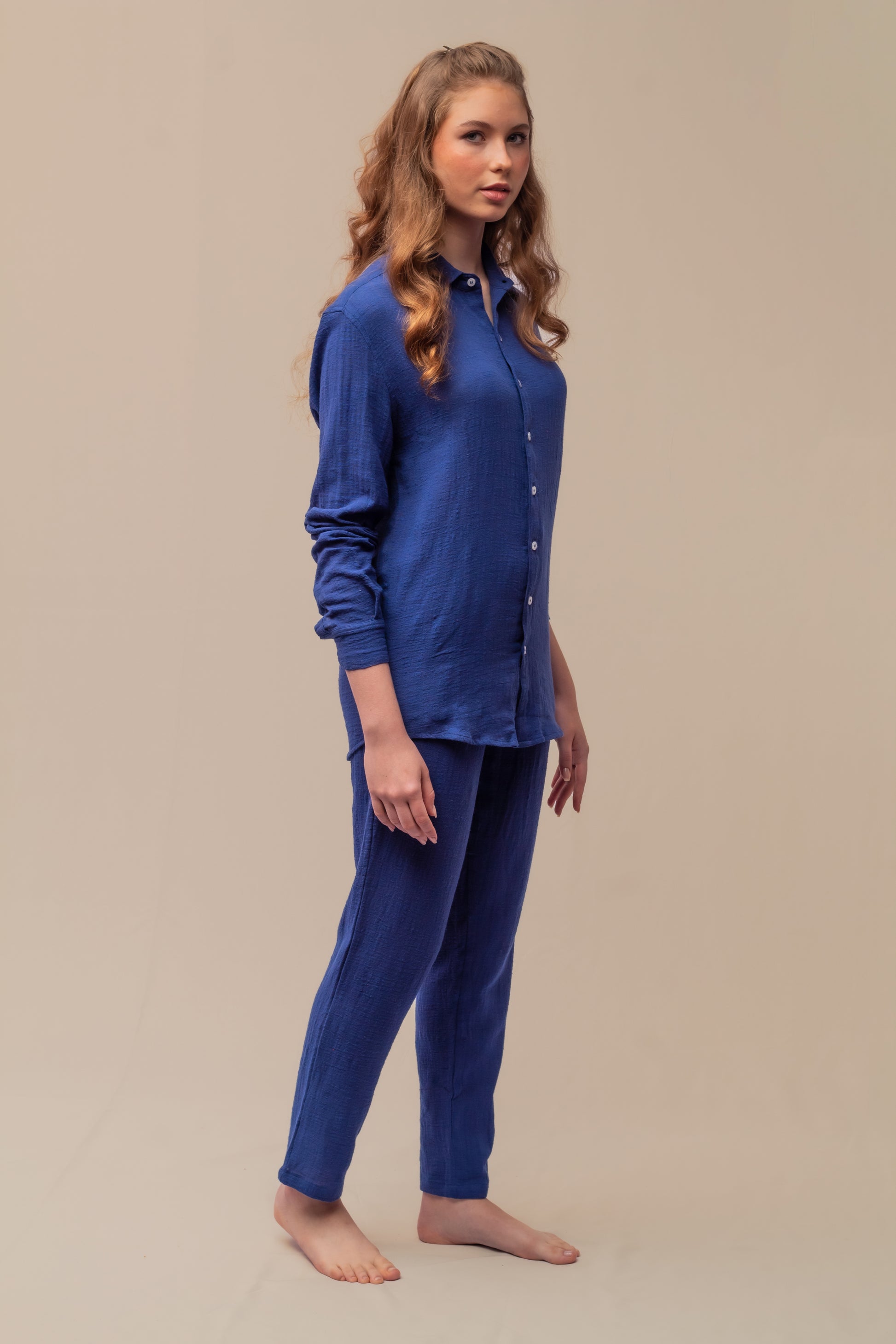 Modelo feminino vestindo full look com camisa manga longa e calça azul marinho unissex em ambiente de estúdio.