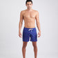 Modelo vestindo Shorts Something Fishy Azul Marinho na praia, com estampa discreta de peixes, vista frontal.