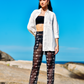 Modelo usando Calça Something Fishy Black com hot pants e camisa aberta, em um cenário de praia.