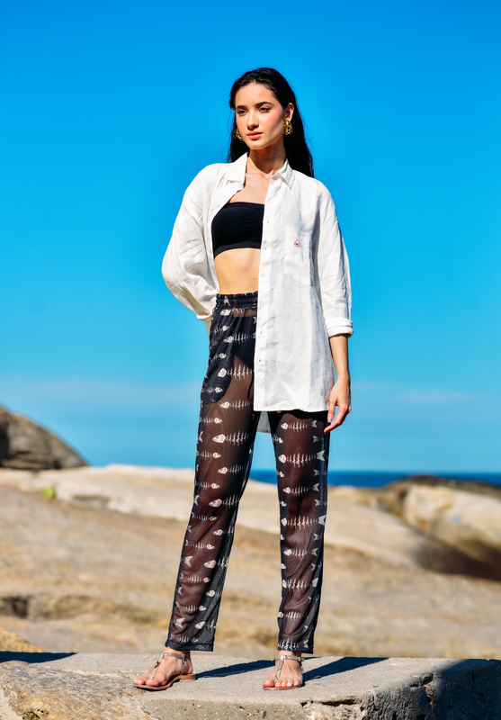 Modelo usando Calça Something Fishy Black com hot pants e camisa aberta, em um cenário de praia.