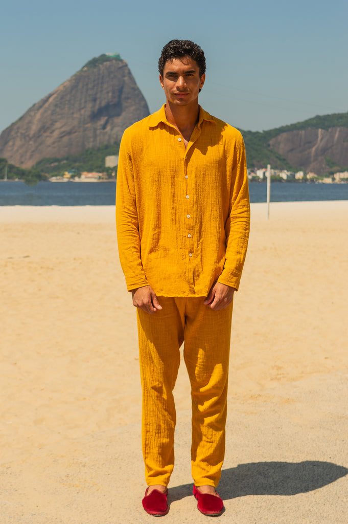 Vista frontal masculino do full look com camisa manga longa e calça amarelo dijon unissex, posando na praia.