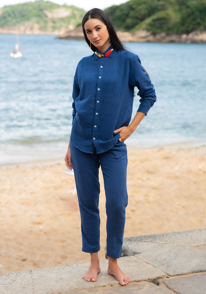 Vista frontal do full look com camisa manga longa e calça azul marinho unissex em modelo feminina, em cenário de praia.