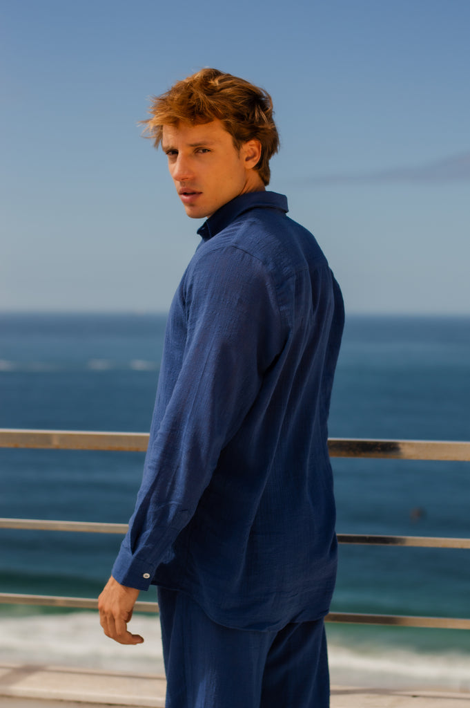 Modelo masculino vestindo full look com camisa manga longa e calça azul marinho unissex, em pose lateral.