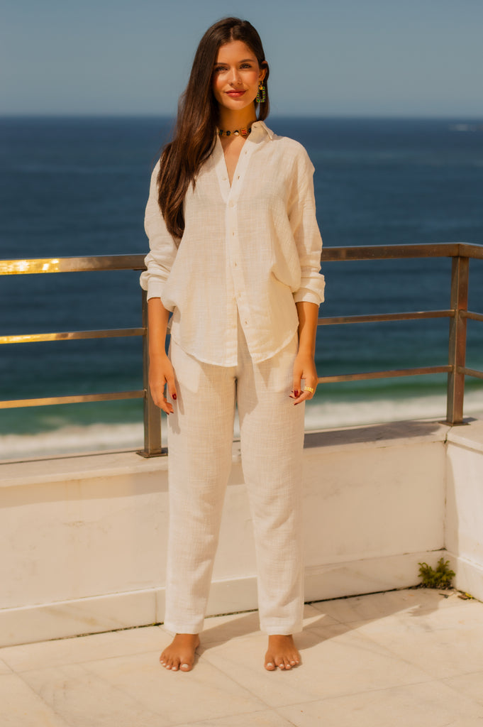 Modelo feminina de frente descontraída vestindo full look com camisa manga longa e calça branca unissex.