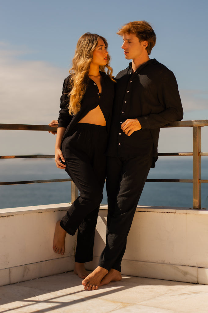 Modelo masculino e feminino vestindo Full Look Preto, camisa e calca casual, unissex, em cenário externo com vista para o mar.