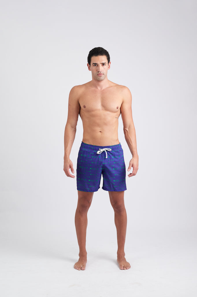 Modelo vestindo Shorts Something Fishy Azul Marinho na praia, com estampa discreta de peixes, vista frontal.