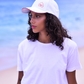 Pessoa usando Boné Parioca Off White 'Love Rio - Live Under the Sun' com logo Rio e detalhes vermelhos, em cenário de praia.