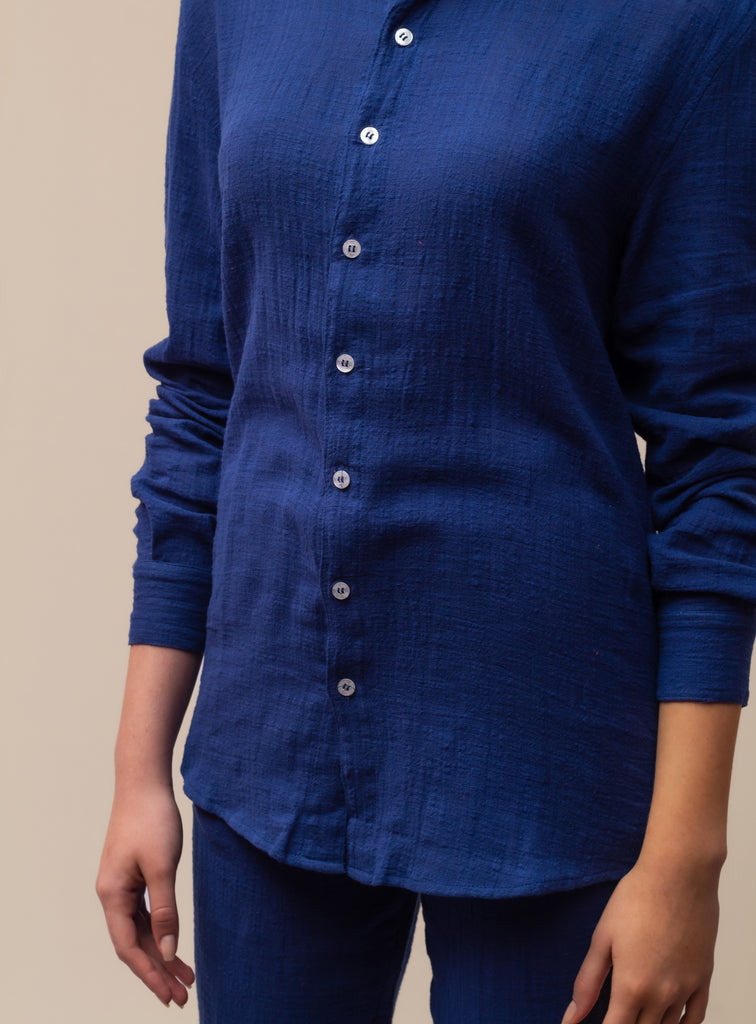 Modelo feminina vestindo full look com camisa manga longa e calça azul marinho unissex em ambiente de estúdio.