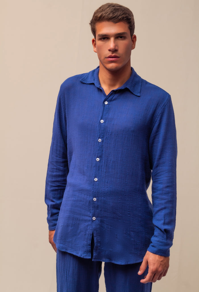 Modelo masculino vestindo full look com camisa manga longa e calça azul marinho unissex em ambiente de estúdio.