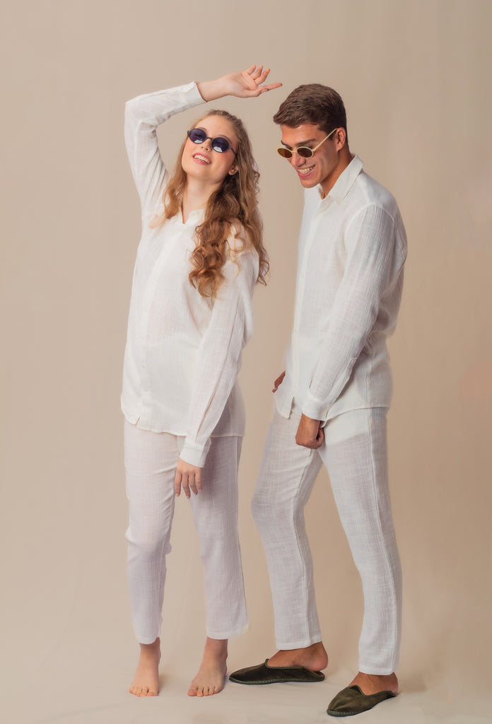 Casal vestindo full look com camisa manga longa e calça branca unissex, em pose casual.