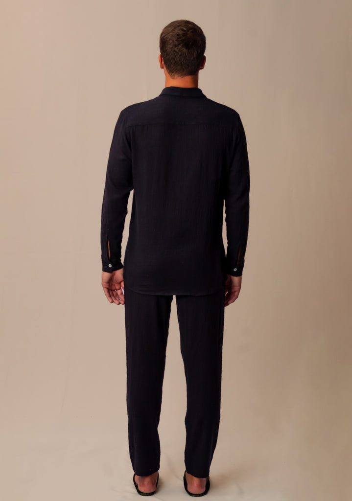 Vista traseira do full look com camisa manga longa e calça preta unissex em modelo masculino, destacando o ajuste confortável.