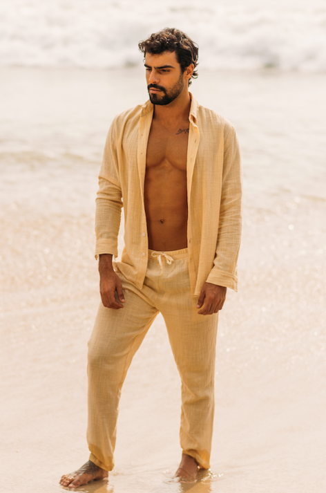 Modelo usando look completo de linho areia concha com camisa de manga longa e calça, em praia.