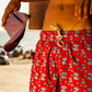 Modelo vestindo Shorts Happy Oyster Vermelho/Azul na praia, vista lateral, destacando caimento e estampa vibrante.
